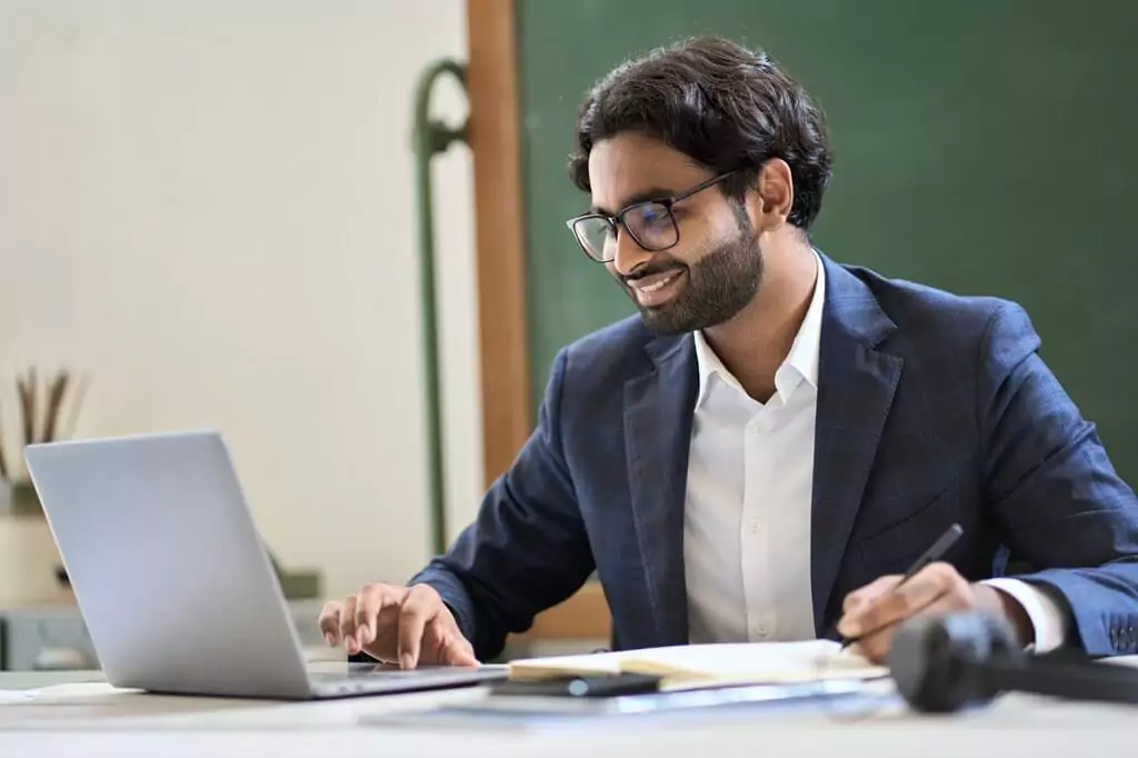 homem sorrindo e fazendo anotações, enquanto usa laptop