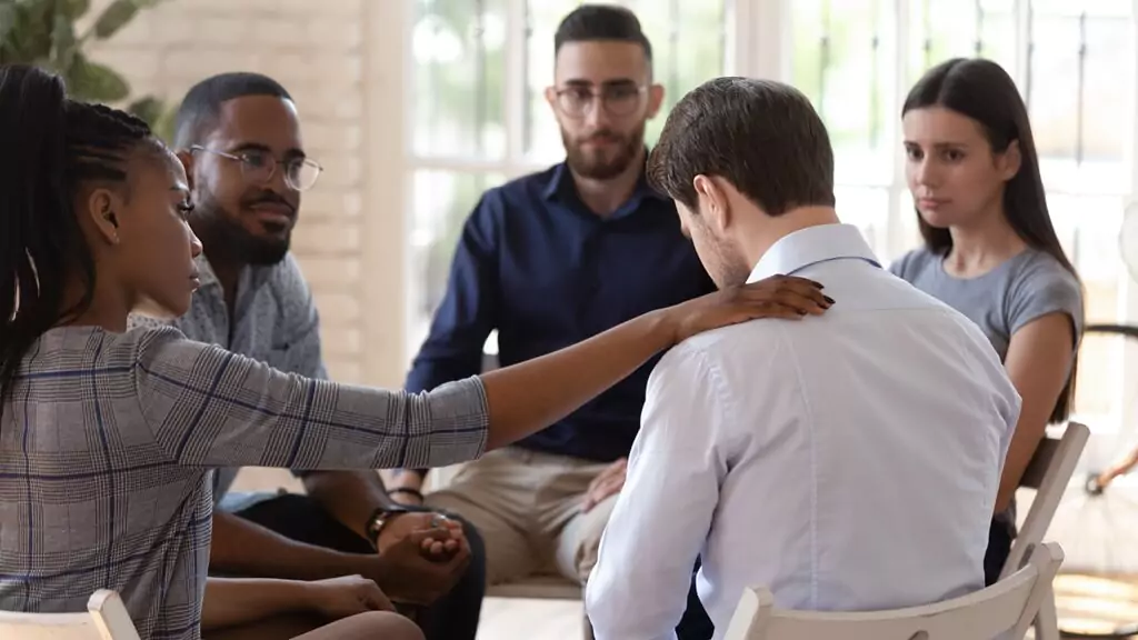 homem sendo consolado por colegas de trabalho